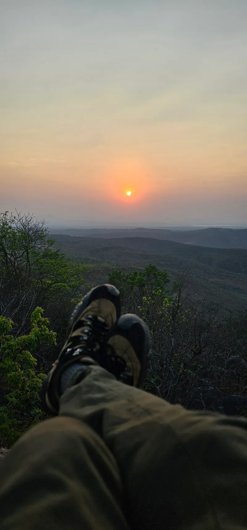 Our shoes resting on the rock at the Halu Chilume Gange viewpoint as the sun sets over the fields